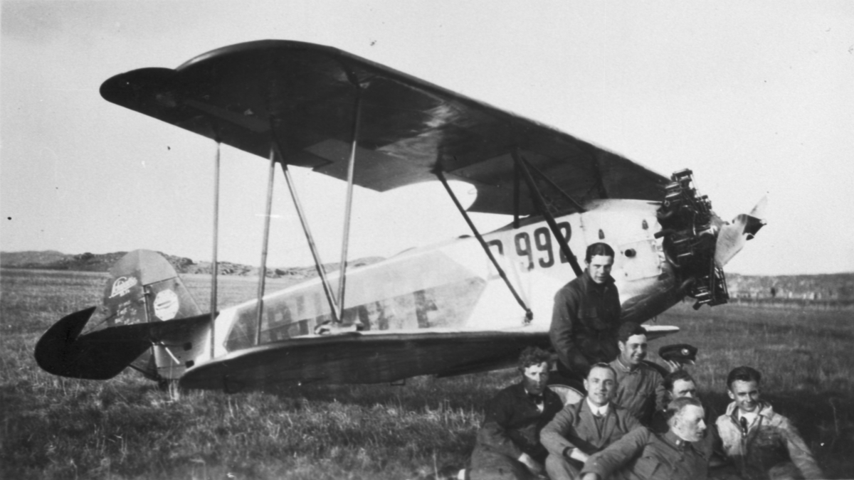 Civilregistrerat tyskt flygplan Raab Katzenstein Kl. 1a nummer D.992 står på ett flygfält. Sju män sitter framför planet i gräset.