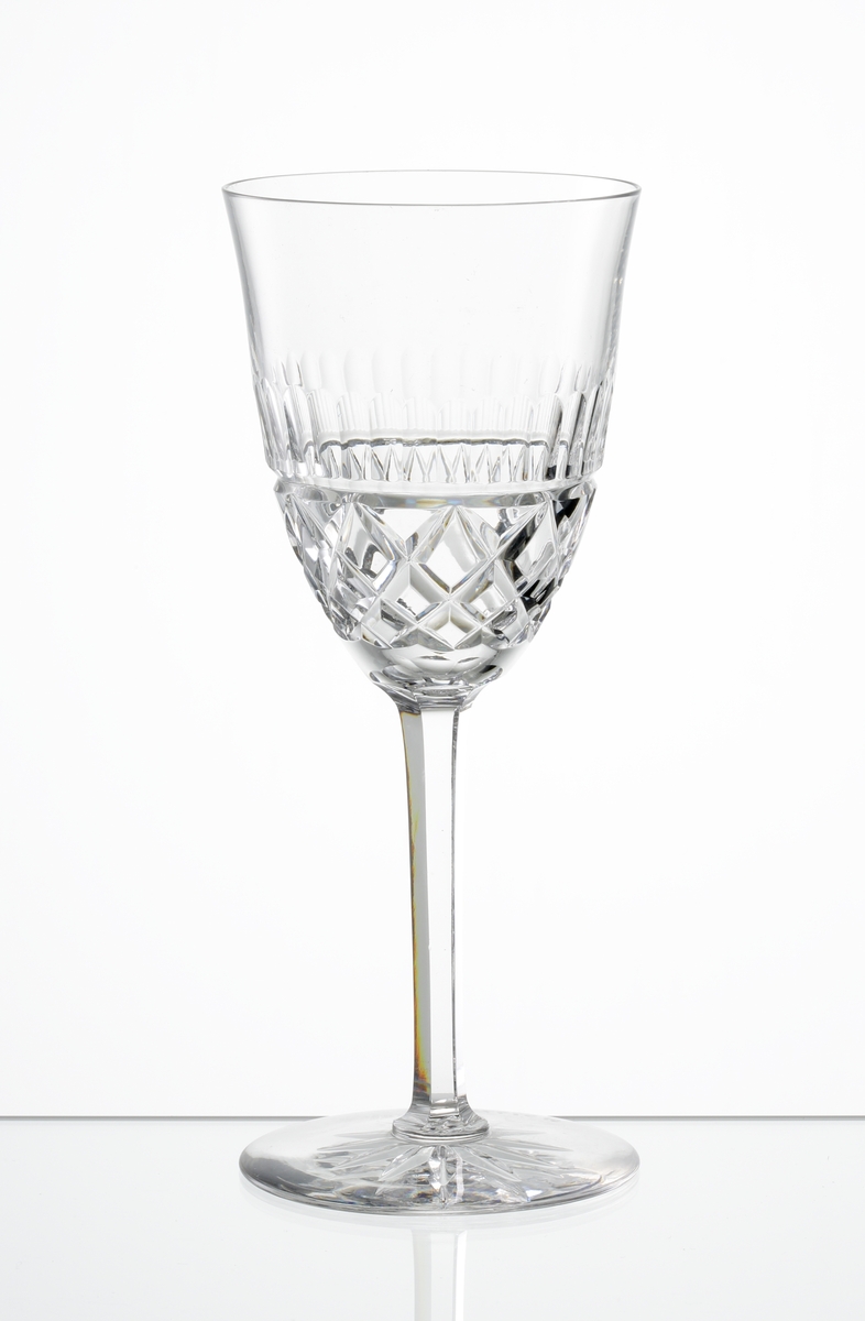 Design: Okänd. 
Vitvinsglas med lätt klockformad kupa, skärslipad nedre del med olivslipad bård. Fasettslipat högt ben. Fot med skärslipad
stjärna i botten.