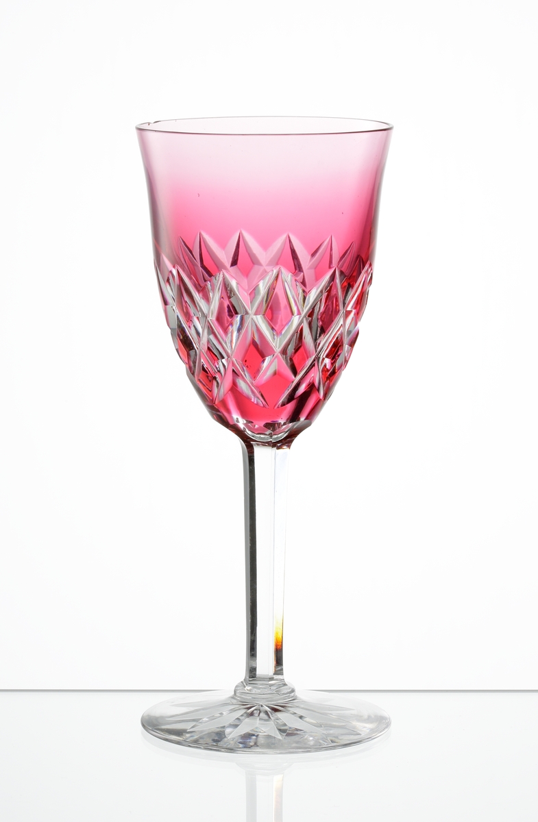 Design: Okänd. 
Vitvinsglas, lätt klockformad, rosatonad kupa med skärslipad dekor, Fasettslipat ben på fot 
med skärslipad stjärna i botten.