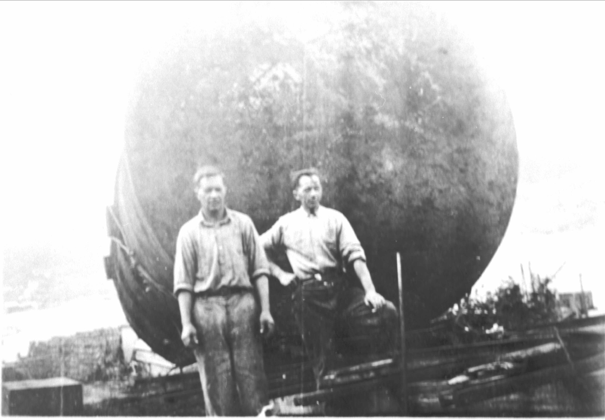 Portrett av to menn foran en stor ståltank.