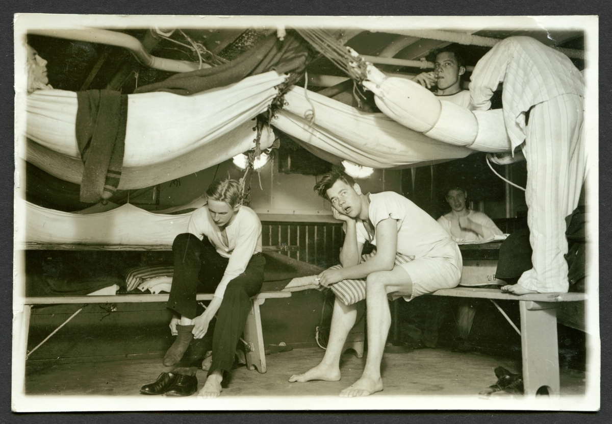 Bilden visar unga sjömän ombord på pansarskepp Svea som håller på att stiga upp på morgonen. En del ligger fortfarande i sina hängkojer, några röker en cigarett och en håller på att kla på sig.