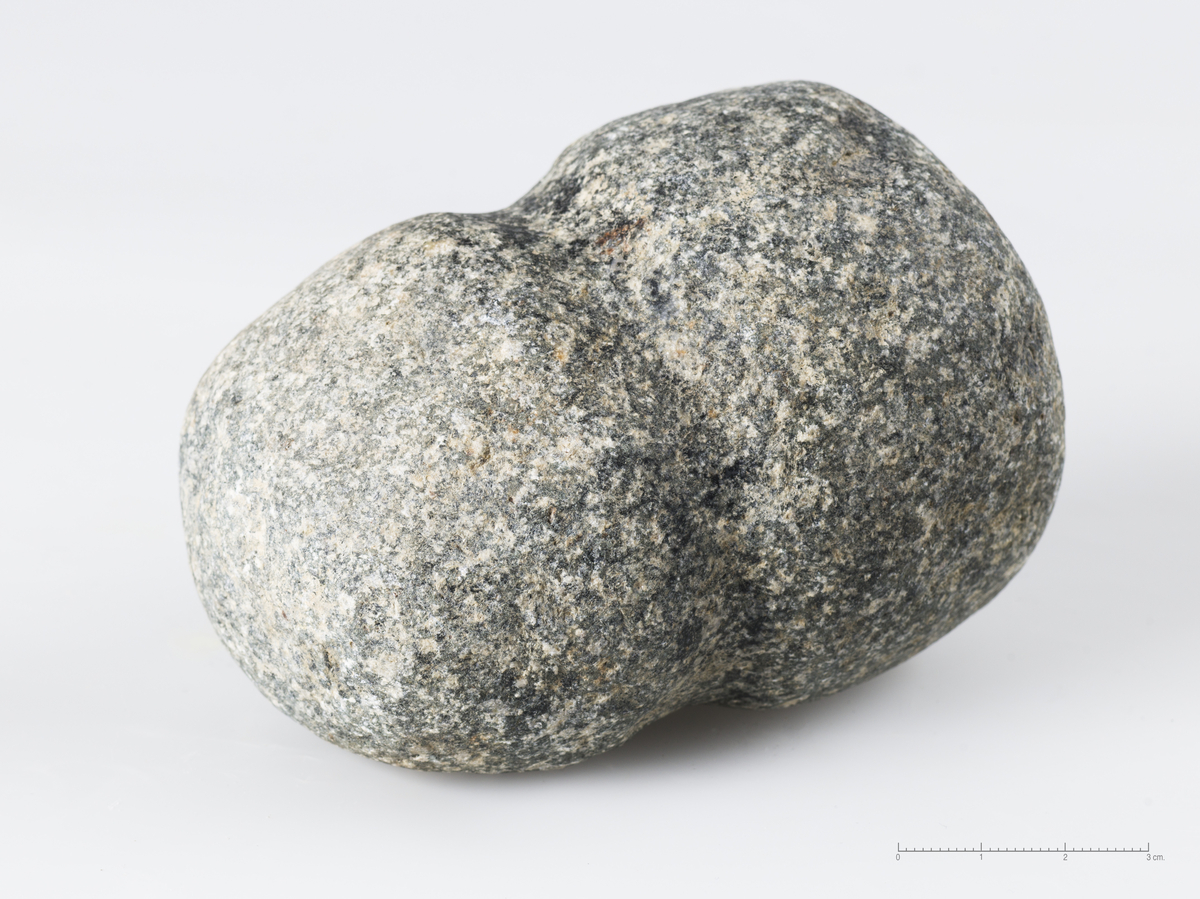 Lodd (?), avlang stein med rundt tverrsnitt, polert/glatt overflate og rundtløpende, tildannet fure på midten. Steinen har naturlig ståflate og smalner av mot en avrundet topp.