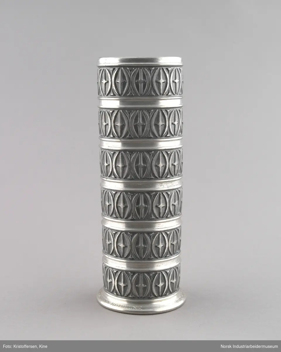 Vase eller pokal fra Tinn kommune til Bondeungdomslaget Maana. Sylinderformet med seks tverrgående inndelinger med ornamental utforming av et kors plassert i ovale sirkler. Mønsteret er repterende.
