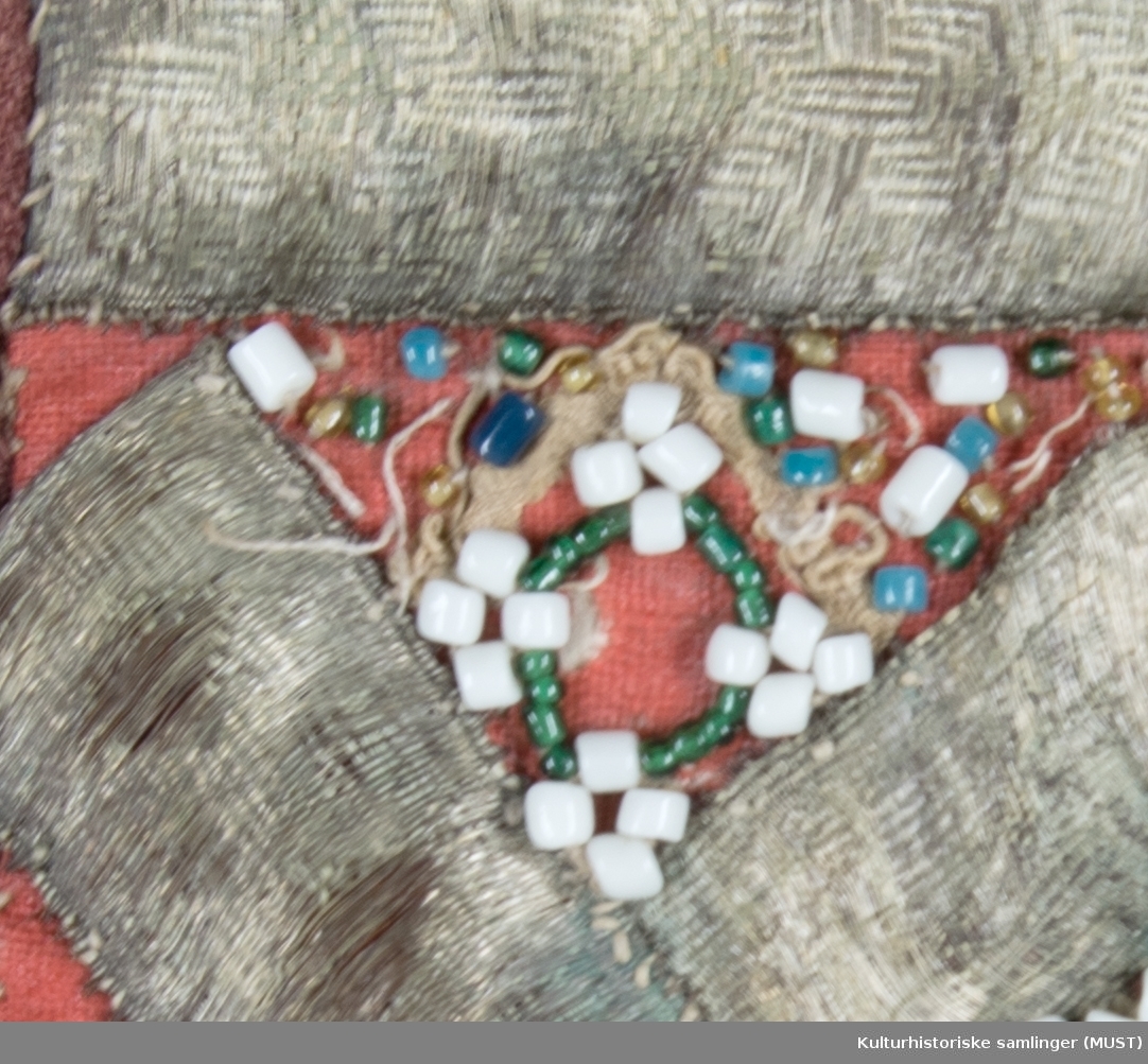 Rød bringeduk med grønn silkekant øverst. Sølvbånd og perler.