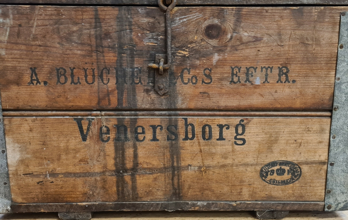 Låda för leverans av flaskor från Blüchers eftr bryggeri.
En metallkrok för att stäna lådan. 
På lådans framsida och baksida finns tryckt:
A. Blucher o CoS Eftr.
Venersborg.