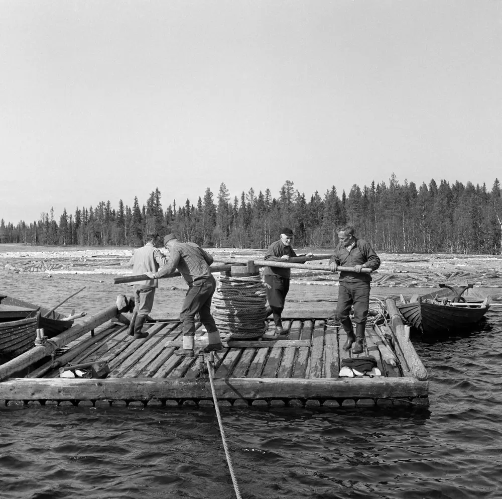 Foto av tømmerflåte med manuell vinsj som betjenes av fire personer.