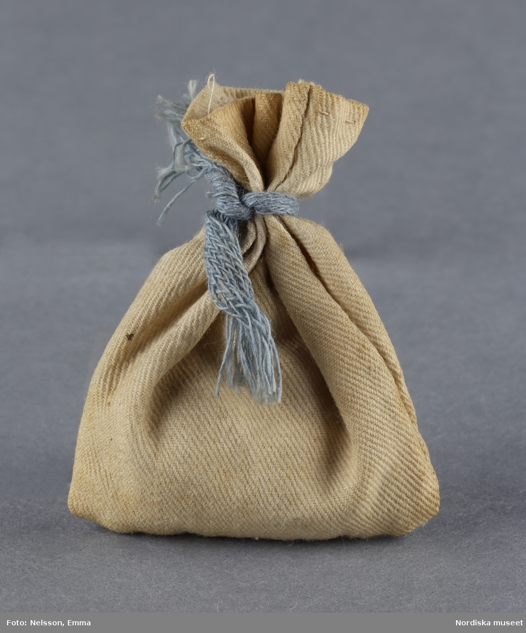 Inventering Sesam 1996-1999:
H  5,5  cm
Säck av ofärgad bomull, handsydd, fylld med papper, omknuten med blått band.
Tillhör dockskåp inv 192.991.
Birgitta Martinius 1996