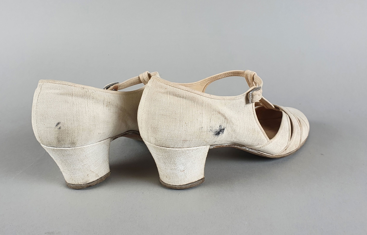 Hvite sandaler av bomullslerret med såle av lær og høye hæler. Spenne på yttersidene.