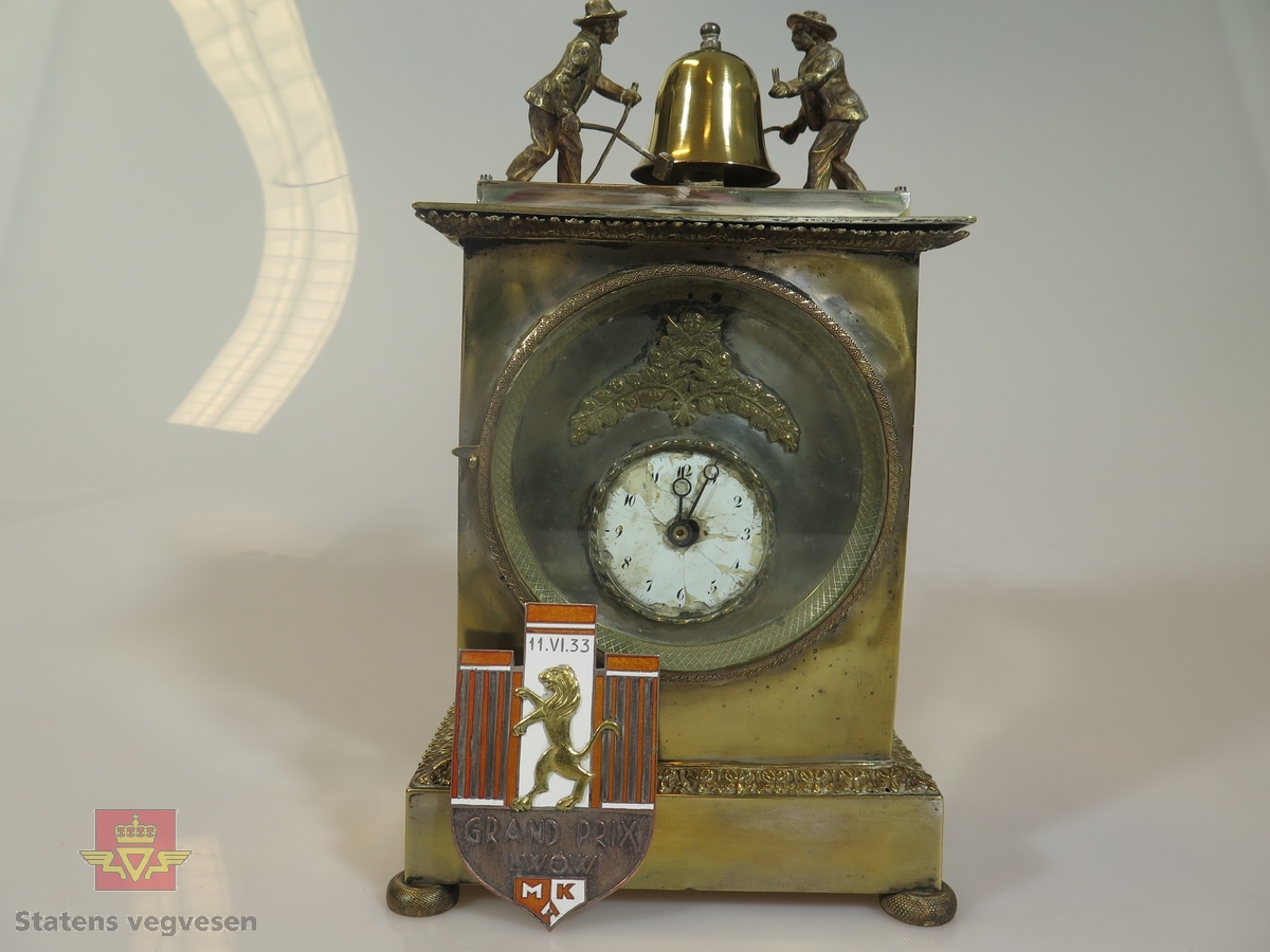 Gjenstandene er en klokke med tilhørende plakett. Klokken er opptrekkbar, Den er dekorert med klokkeslagere og innskrift. Plaketten har et motiv med en løve samt påskrift.