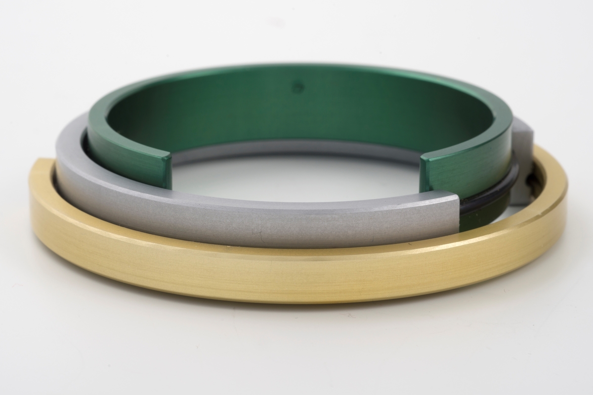 Sirkulært armsmykke bestående av tre ringer av eloksert aluminium lagt utenpå hverandre. Ringene, som er åpne, er litt forskjøvet i forhold til hverandre, slik at de sammen danner en lukket form. Mellom ringene er det lagt tynne gummistrenger. De to innerste ringene, grønn og aluminiumsfarget, er noe bredere enn den ytterste, gullfargete ringen.