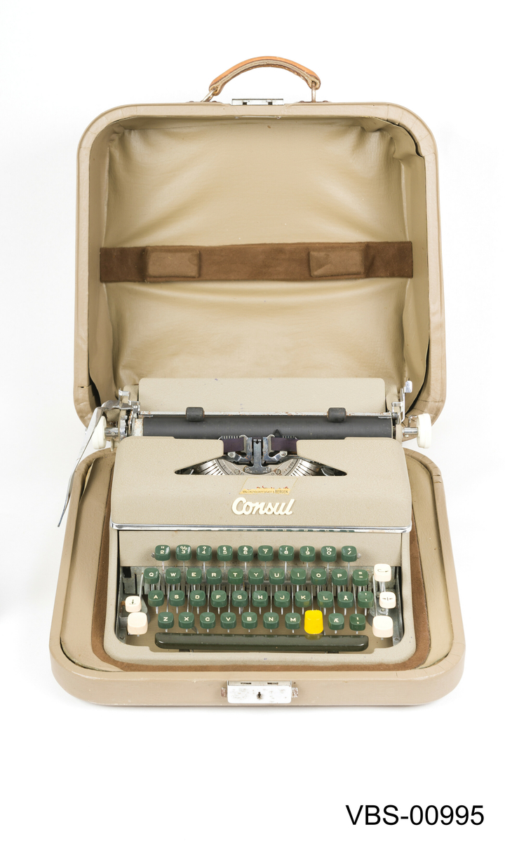 Reiseskrivemaskin i koffert.
Transportabel skrivemaskin i metall og plast. Skrivemaskinen er fastmontert i koffertbunnen, men kan den tas ut av kofferten. Den har avtagbart lokk med bærehåndtak i lær. Nøkkelløs lås.