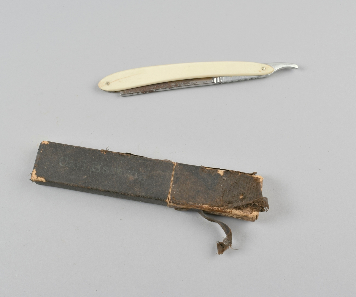 Sammenleggbar barberkniv med skaft i benmateriale, i futteral av papp kledd med tekstil.