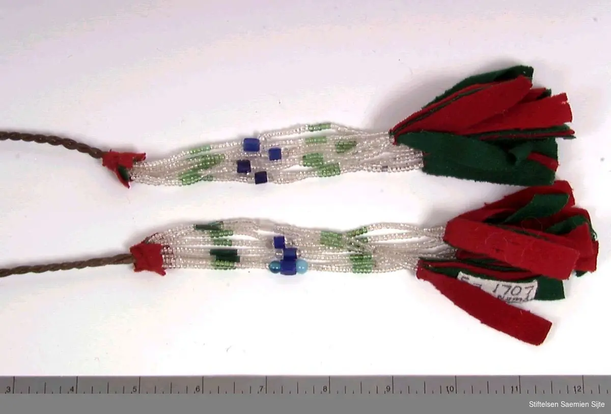 Skinnsnor mes to store og dekorative klaser med perlesnorer avsluttet med store tekstillapper i rødt og grønt.