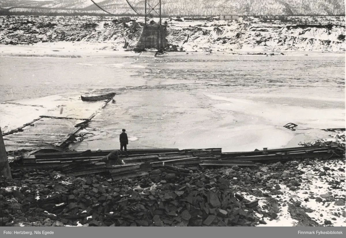 Arbeidet foregår på Tana bru, 1947. Gamle brua ligger i elva. En mann står ved stranden.  vi ser rester av tårnet på østre side. Se også bildene 280-312.