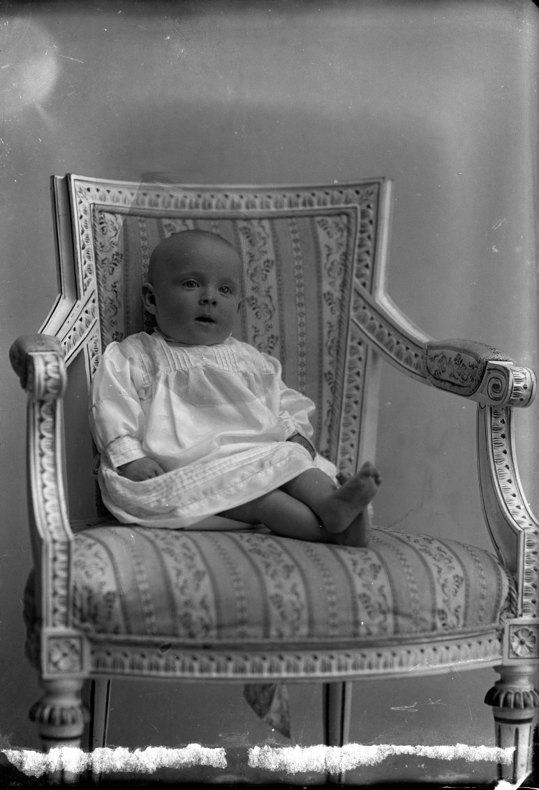 Ett spädbarn sitter i en stol i gustaviansk stil. Det är "flickan Hagström", i Bunnström.