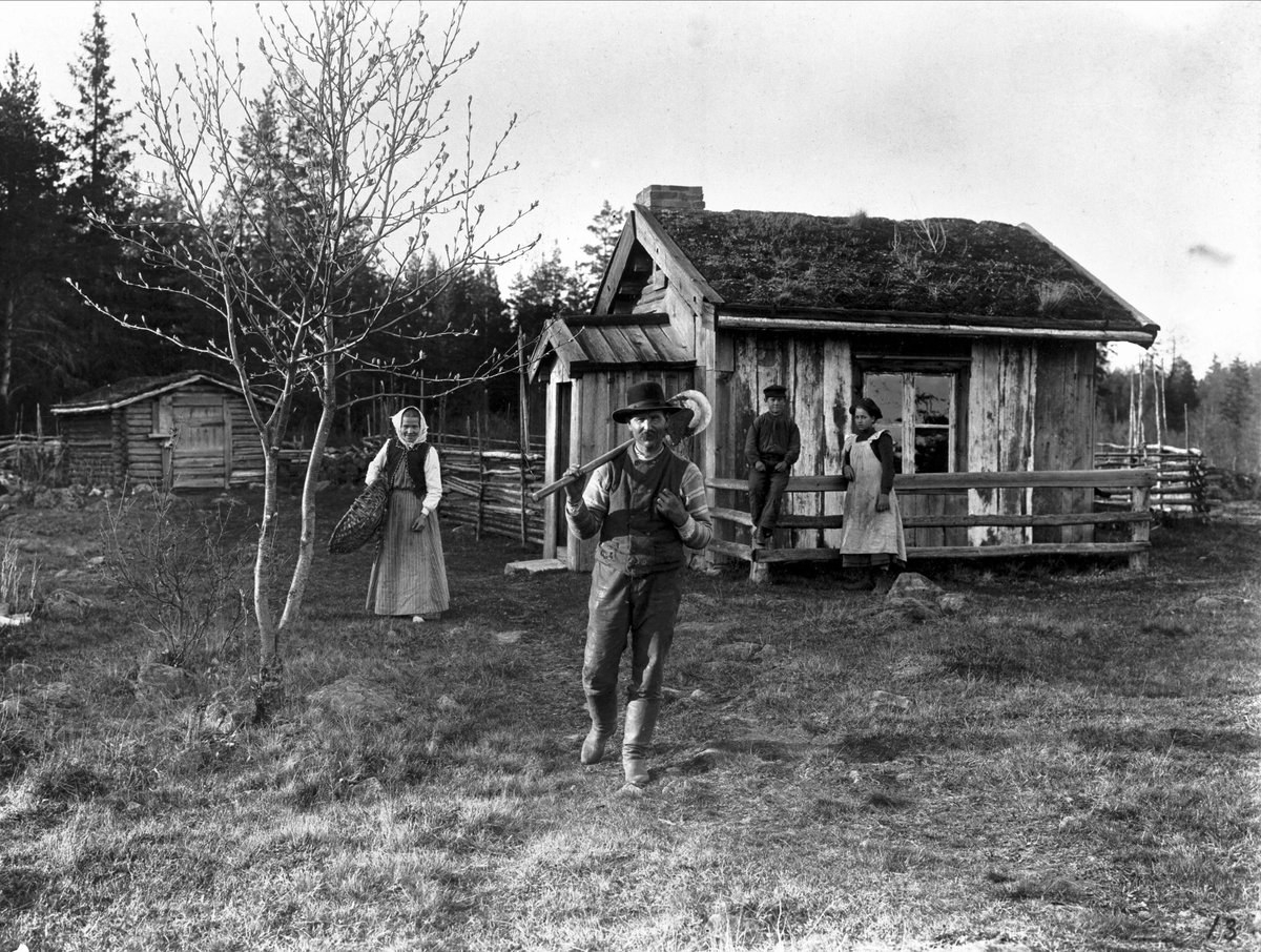 Torpare, Västergötland. En man en kvinna och två lite äldre barn, en pokjke och en flicka utanför ett litet torp. Mannen bär en spade , kvinnan en korg.