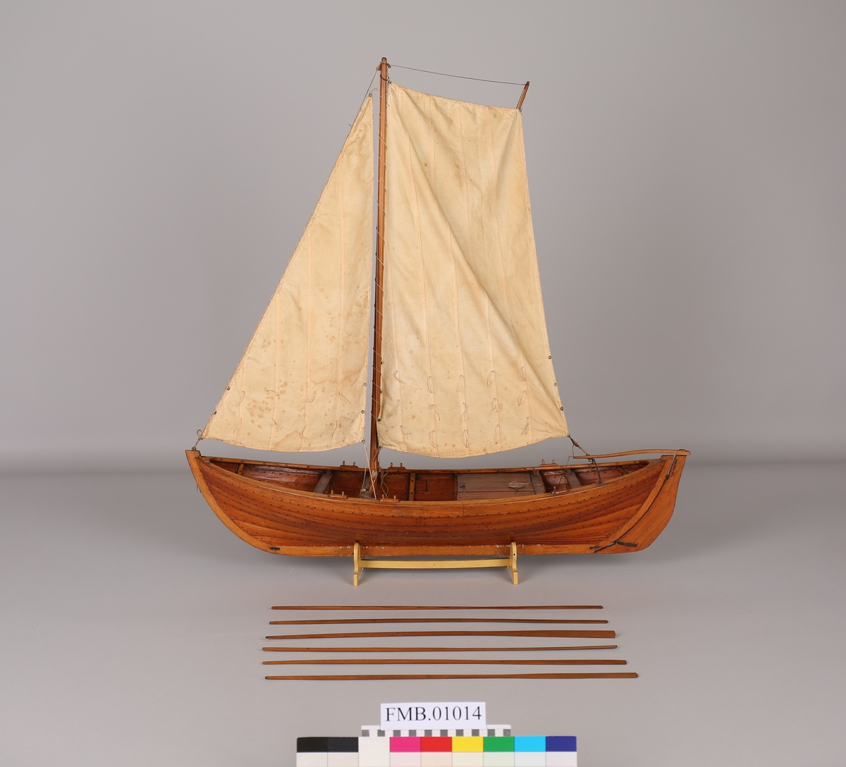 Modell av fiskebåt med brønn med  mast og 1 rombeformet seil og 1 trekantet. Tvers over båtens akterende er en stang hvor det rombeformete seilet er festet og som rorstangen kan hvile på.