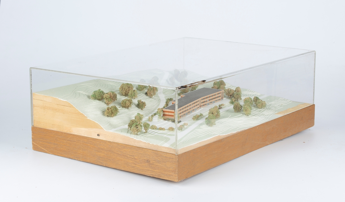 Modell av planlagt næringsbygg i terreng (Oksval, Nesodden). I kasse av klar plast.