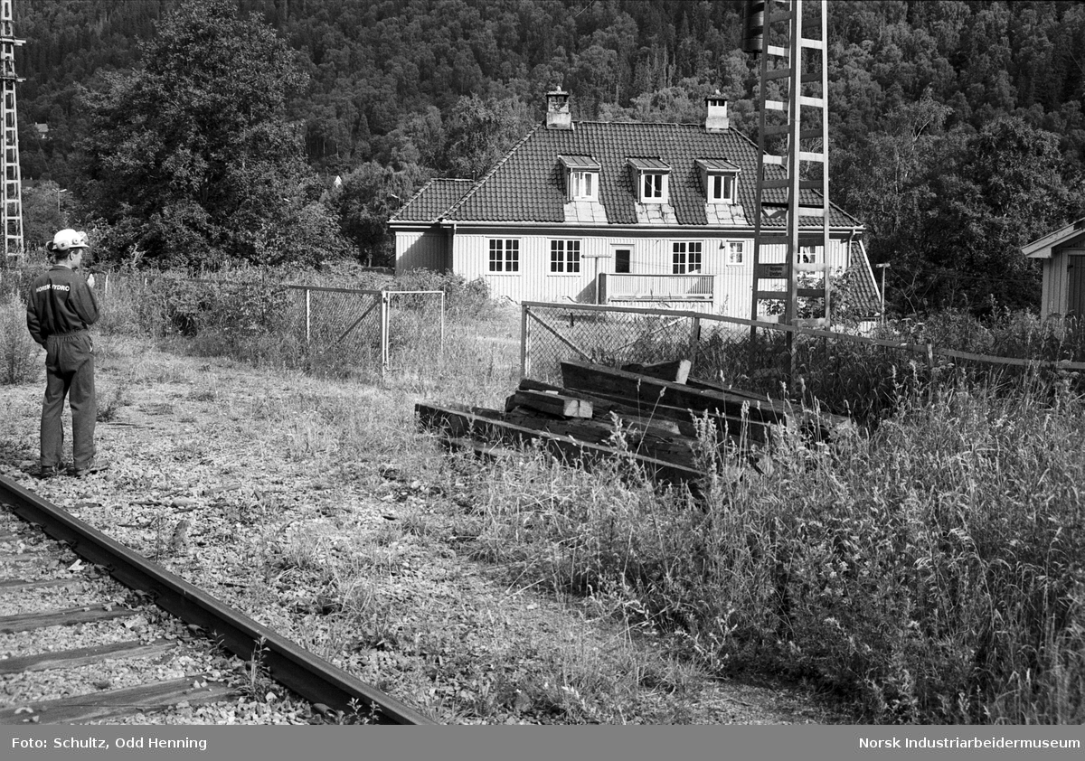 Sviller som ligger lagret, og en mann i arbeidsklær fra Norsk Hydro, på stasjonstomta. Nedenfor en bygning på Jernbaneplassen.