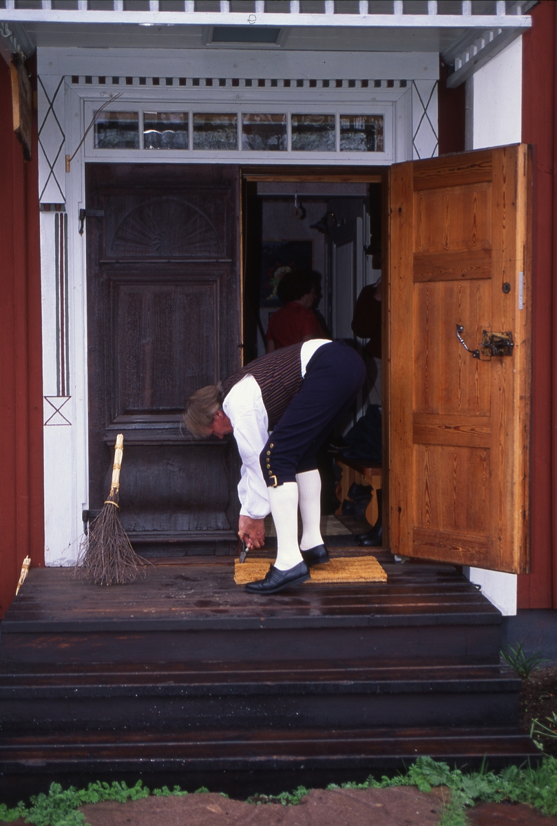 Hilding klädd i hembygdsdräkt står böjd framför dörröppningen på gårdens förstukvist. Han håller en tång i handen. Reportage på Sunnanåker, maj 1991.
