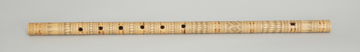 Sylindrisk fløyte av bambus i et stykke. Dekorert med innrissete stiliserte border og brennemerker, seks fingerhull brent inn i røret.