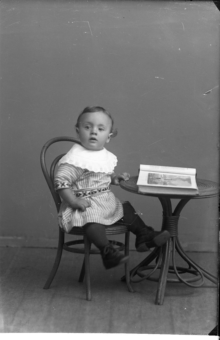 Porträtt av en liten pojke som sitter i en barnmöbel med en bok uppslagen på bordet.