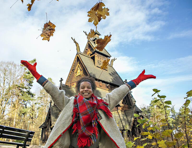 En kvinne kaster høstløv opp i luften foran stavkirken. (Foto/Photo)
