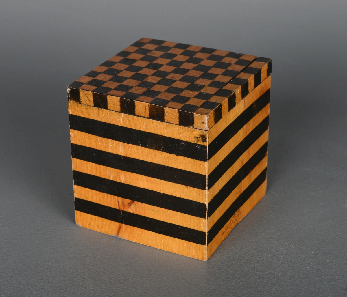 En kube av tre som ligger i en metallboks med lokk. Det ser ut som en 10cm3 kube, men den er ikke helt nøyaktig når man måler den. Den er satt sammen og limt litt ujevn. Kuben har sorte ruter i sjakkmønster av kvadratcentimeter på toppen og på øverste del av to av sidene. En av de øverste radene med 10 biter a 1cm3 kan tas ut. På to av sidene er det 1 centimeter brede linjer, men den nederste linjen er 1,3 cm bred, høyden blir 10 cm til sammen, men linjene er noe ujevnt plassert. Dybden og bredden er 9,6 cm. De tre andre flatene er blanke. Kuben er et visuelt hjelpemiddel for å anskueliggjøre hvordan man måler volum. Metallboksen er akkurat stor nok til å få plass til kuben.