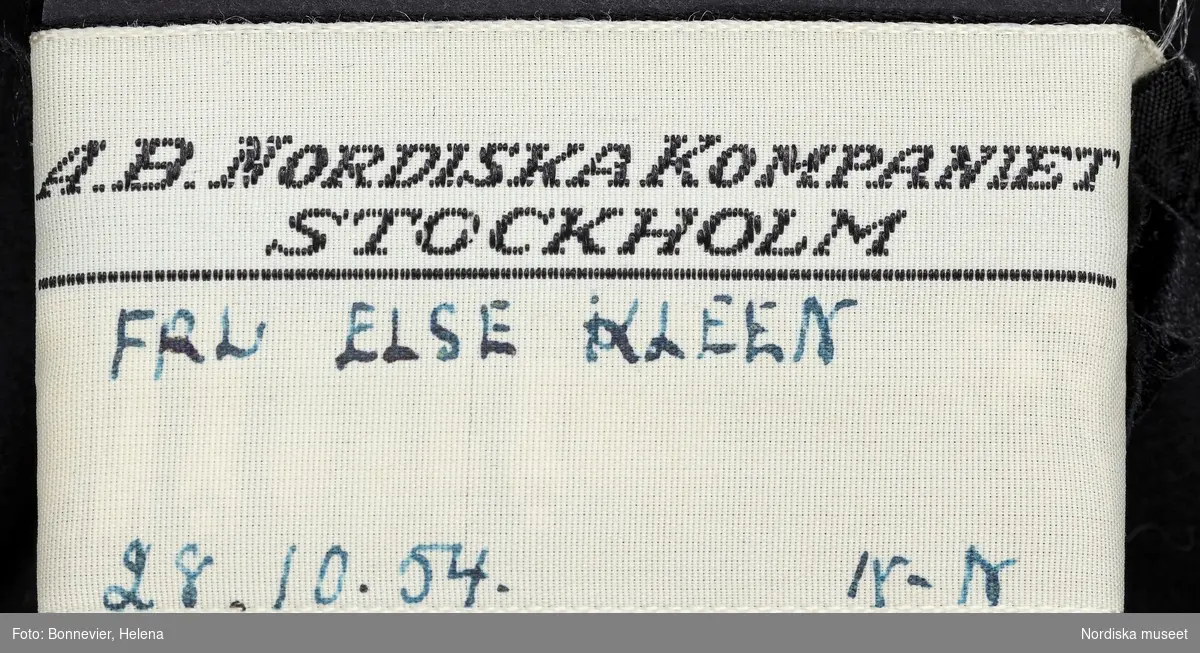 Svart sidenklänning med vit krage och manschetter. Beställd från NK:s Franska damskrädderi av Else Kleen Möller (1882-1968), samhällsdebattör och modejournalist. Levererad oktober 1954.