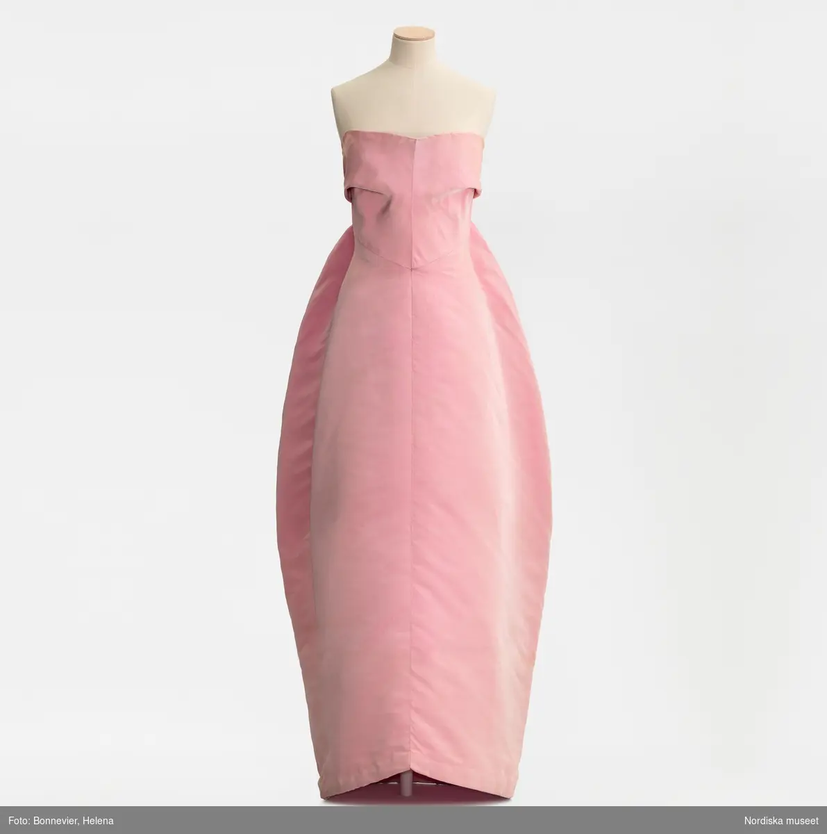 Klänning monterad på docka. Originalmodell från Cristóbal Balenciaga i rosa sidenfaille som visades på NK:s Franska damskrädderi. Karin Ellhammar (född 1938) erbjöds att köpa originalet i slutet av säsongen, hösten 1960. I Röhsska museets samlingar, RKM 40-1999.