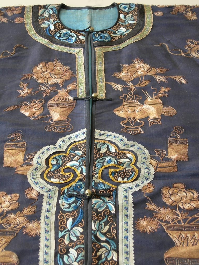 Kvinnojacka, troligen använd av mandarinhustru som ämbetsdräkt. Bärs vanligen tillsammans med byxor eller veckad kjol.

Blåsvart sidentyg, tuskaft. Rak ärm.
Fram- och bakstycke dekorerade med guldbroderi, läggsöm sydd med tvärstygn, roströd silketråd. Guldtråden är gjord av pappersguld virad runt en silkekärna. Vissa mönsterformer har en klassisk symbolik, t.ex. ärtskidan för fruktbarhet, andra former är av mer dekorativ art.

Dekorativa band runt framkant, nederkant och sprund. Ytterst ett kantband i blått siden, därefter ett band, silkebroderi, 3,5 cm, blommor och cirklar i vitt och olika blå nyanser samt guldbroderi, innerst ett mönstervävt band, 2 cm brett. I halsringningen ytterst ett kantband i blått siden, därefter ett band med silkebroderi, likadant som på kantningen runt nederkanten, därefter en snedremsa i siden, ca 1 cm bred, och innerst ett mönstervävt band, 1,5 cm brett.

På ärmen snedremsa i blått siden, ca 1,5 cm bred därefter band i silkebroderi likadant som runt nederkant och halsringning. Ytterst ett tyg, 12 cm brett, dekorerat med mönstervävt band i blått och guldfärg. Tyget är broderat? med tråd i liknande färg som tuskaftsbottnen. Åtdragen plattsöm som bildar mönster tillsammans med den något grövre tråden. Symboliska mönsterformer, de 8 taoistiska symbolerna, bl.a. flöjt, solfjäder och lotusblomma mellan dessa dekorativa mönster, S-formade. Ärmens baksida och ca 1/4 av framsidan täckt med guldbroderi, läggsöm sydd med tvärstygn, guldfärgad tråd, och detaljer i silkebroderi, svart, vitt och lila, platt- knut och klyvsöm. Mönstret föreställer bl.a. vattenströmmar, vågskvalp och en drake som stiger upp ur vattnet. Draken har 4 klor och symboliserar den näst högsta rangen, den högsta har 5 klor och det är kejsarens symbol. Draken är en positivt laddad symbol, en manlig symbol.

Jackan knäpps med tre klotformade mässingknappar och öglor gjorda av svarta, runda band.
Foder: ljusblått siden.

En märkning på höger framstyckes insida i halsringen, kinesiska tecken skrivet på tyget och på en vit klisterlapp.