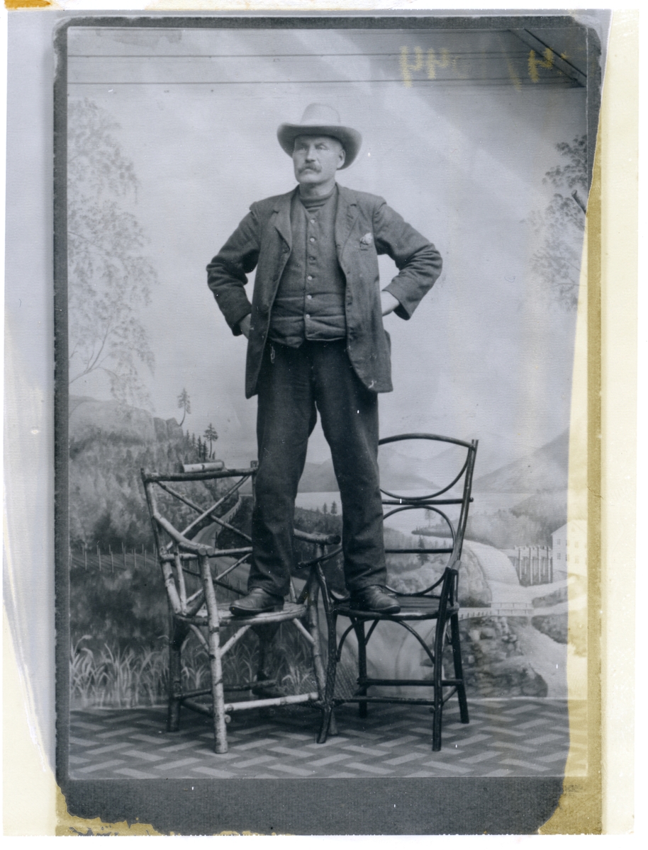 Portrett av ein mann som står oppå to stolar. Han har ein cowboyhatt på hovudet.