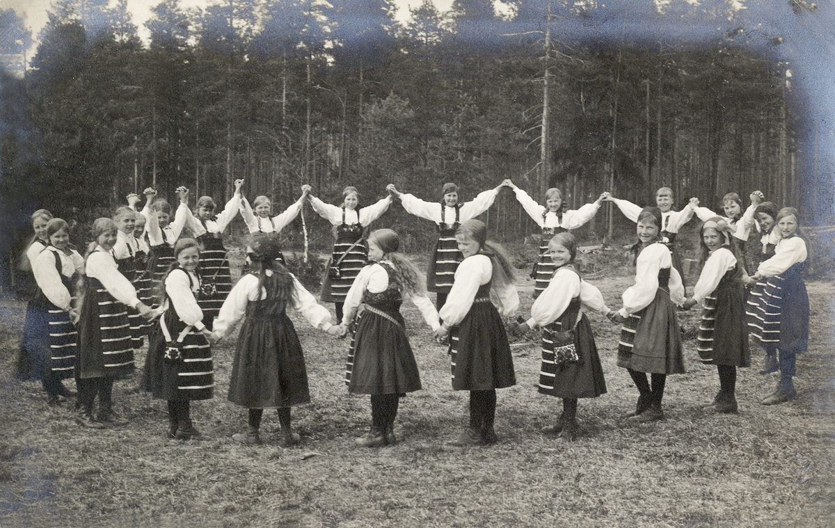 En grupp småflickor i Rättviksdräkt har samlats i en ring utomhus, ca 1910.