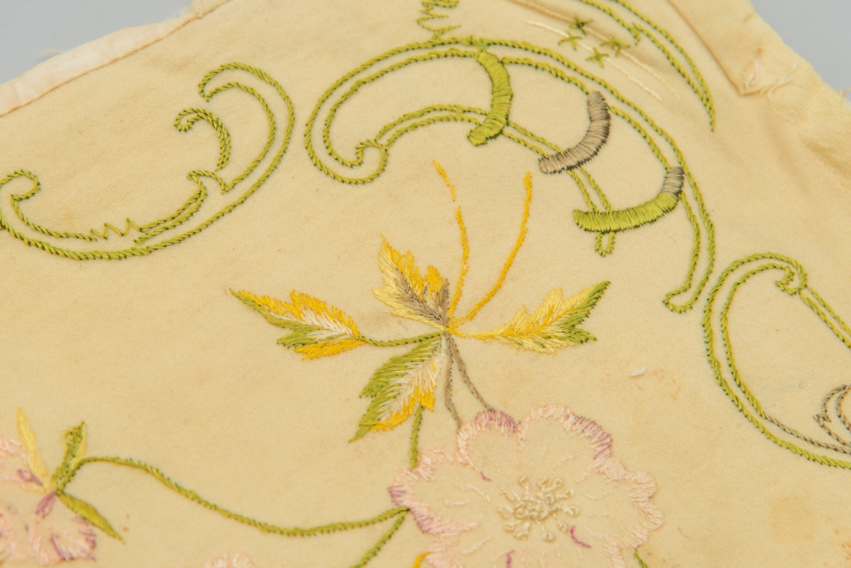 Duk med bølgete detaljer i kantene. Dekorativt broderi i grønt i tillegg til blomsterbroderi.