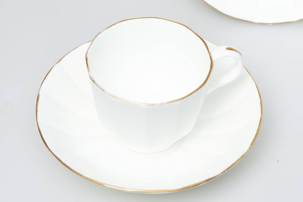 Kaffekopper i tynt porselen. Både koppen og skåla er 12-kantet. Skåla er ganske stor i forhold til koppen. Gullkant på både kopp og skål, samt på hanken. Det er enkelte veldig små blå prikker i porselensmassen. Serviset er umerket.