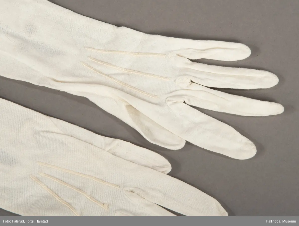 Et par hvite bomullshansker med to lyse, runde perlemorstrykknapper på hver hanske.