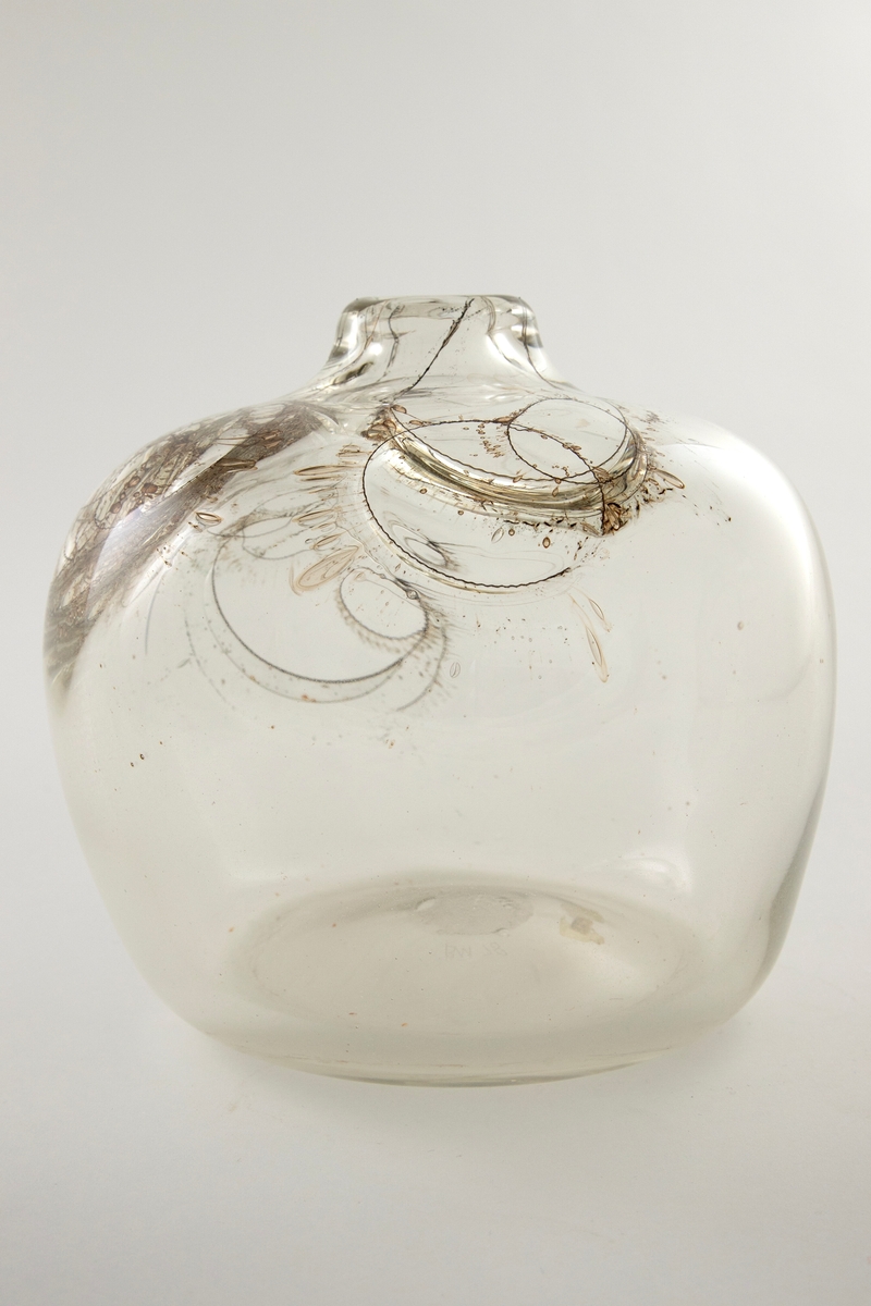 Flattrykket kuleformet vase i klart glass med kort hals. Korpus er dekorert med innlagte ringer av metalltråder på vasens øvre halvdel, og ut ifra disse stråler lange, spisse luftbobler. Puntemerke under vasens bunn.