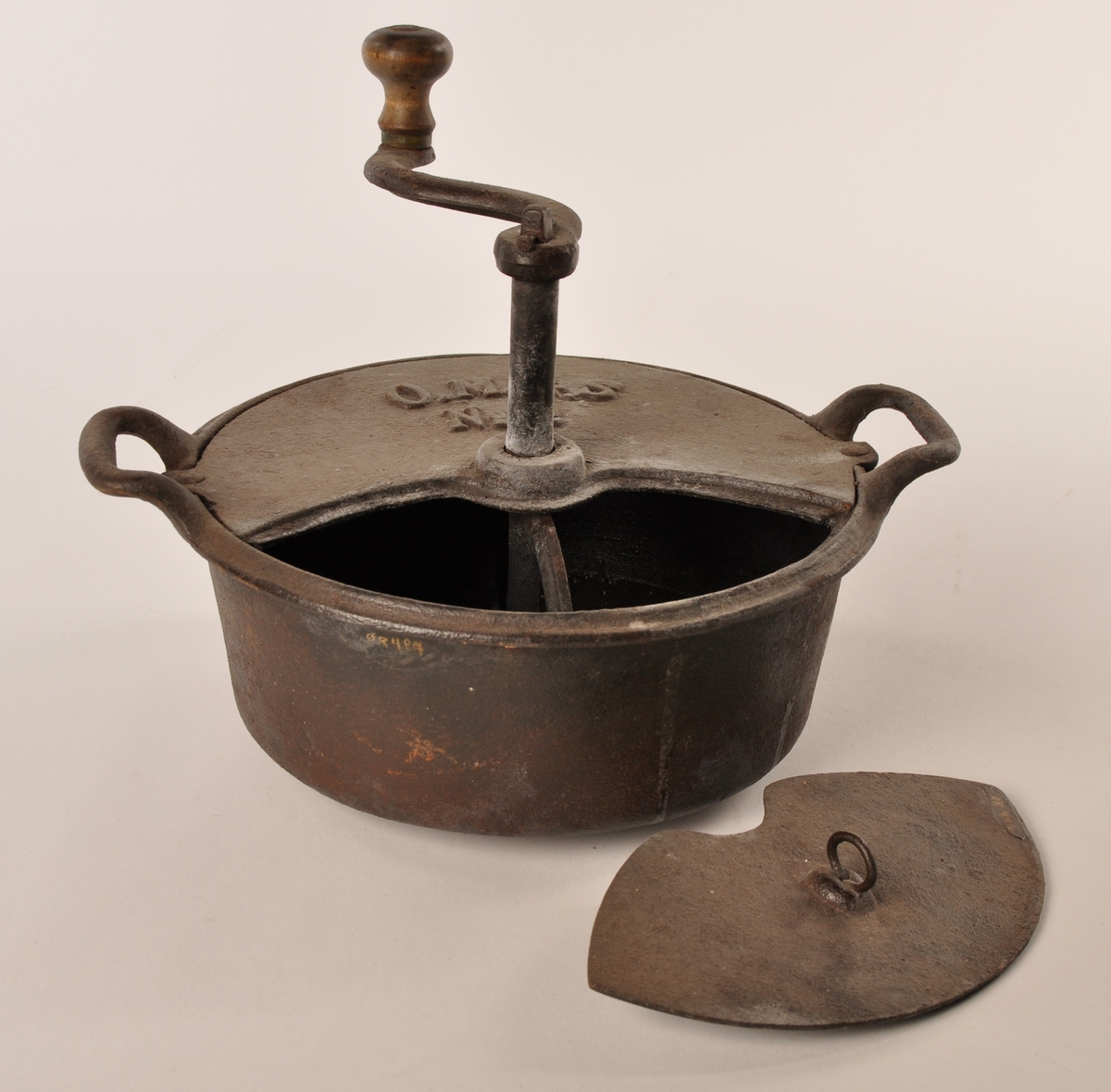 Rund kaffebrenner av jern med to hanker og delvis avtagbart lokk, sveiv i jern med trehåndtak. På lokket O. M. &. S No 2