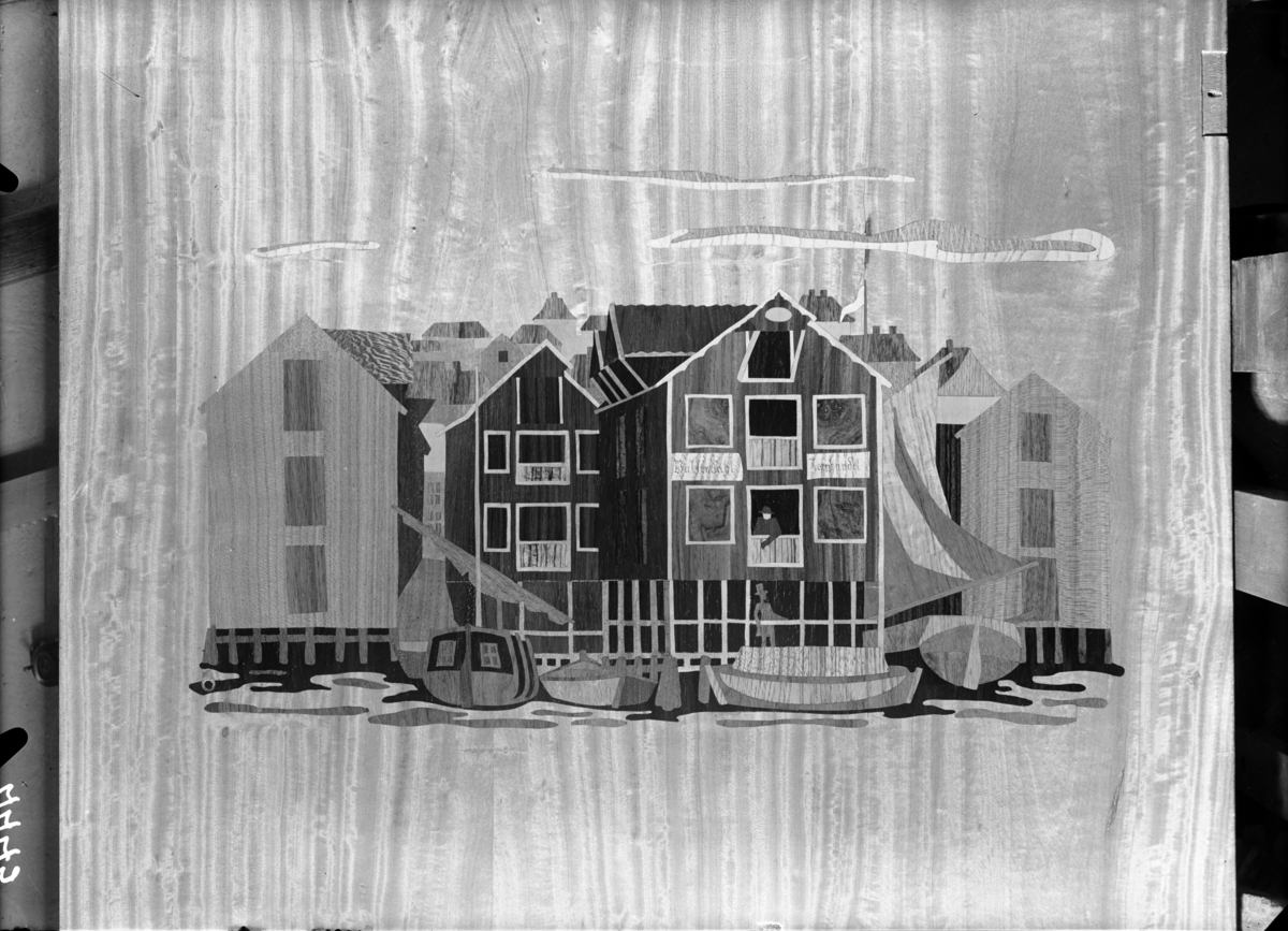 Bilde på treplate med dekor i intarsia, motivet er en havn med mennesker, hus og båter fra "gamle dager". Publisert i Bonytt, trolig 1949-55.