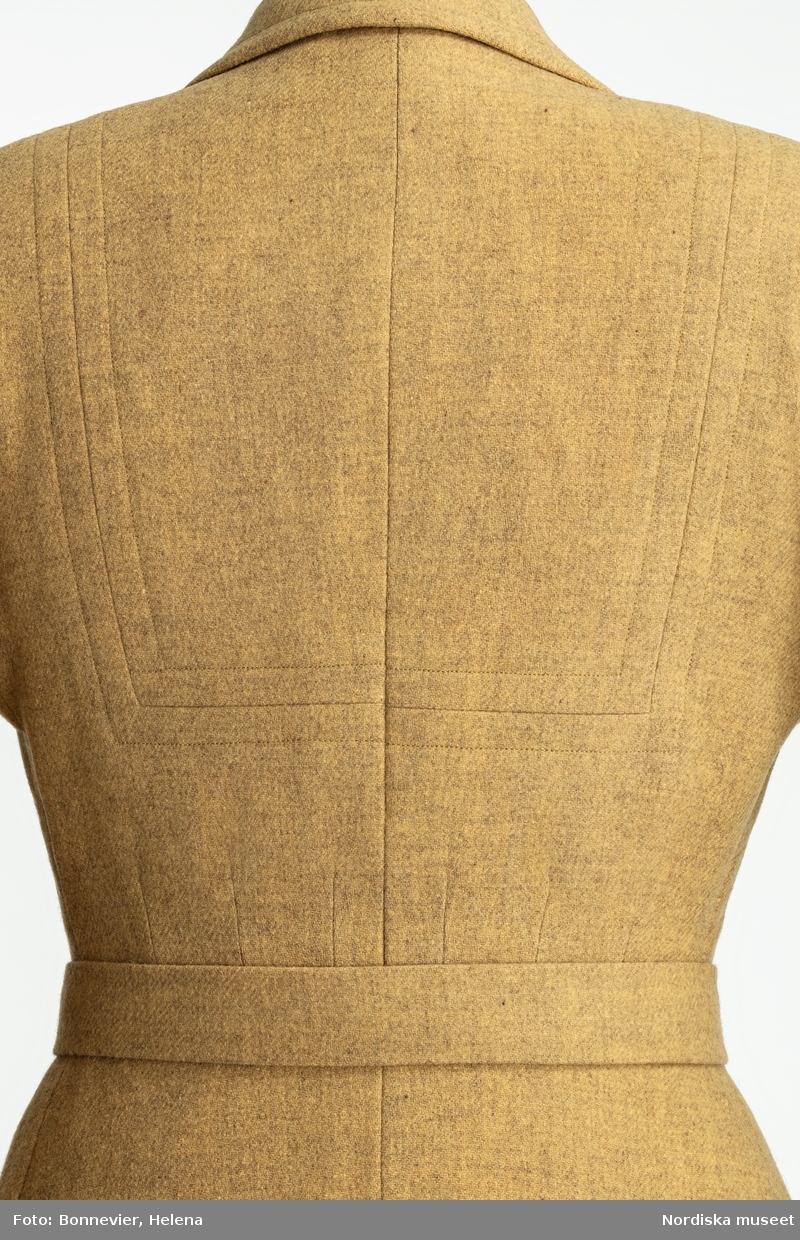 Uniformsinfluerad yllekappa i tidstypiskt snitt med uppbyggda axlar. Beställd från NK:s Franska damskrädderi av Astrid Lamby född Trana (1898-1990). Levererad mars 1944.