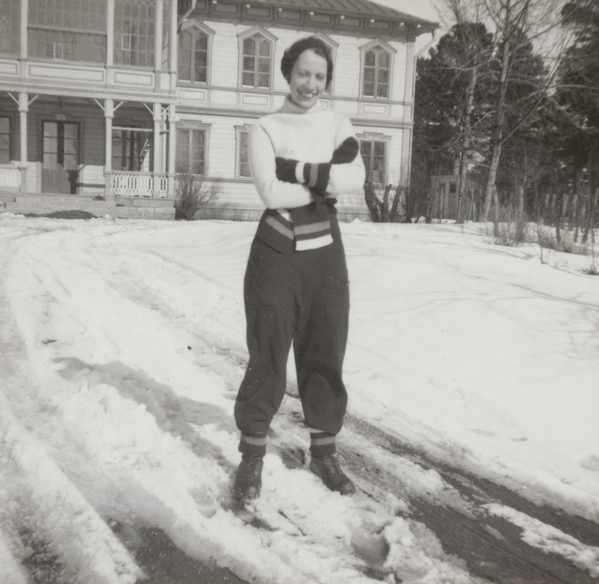 Porträttfoto av Anna Linderstam i skidklädsel utanför byggnad, vintertid, cirka 1925. Helbild.

Text vid foto: "'Annika gillar 'Östran'"