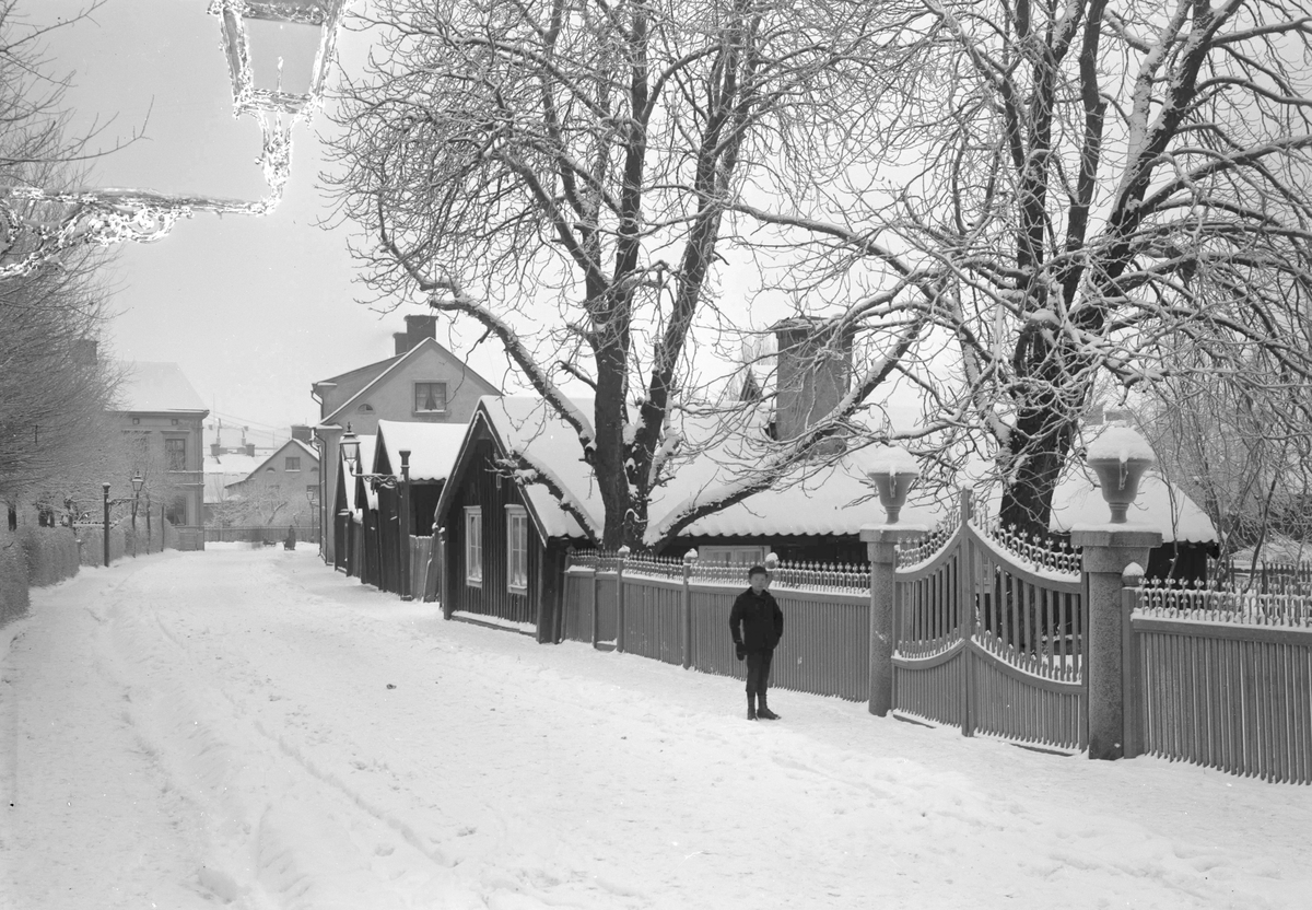 Vinterbild från Djurgårdsgatan i Linköping. Tiden är omkring förra sekelskiftet. Pojken på bilden står framför ingången till den så kallade Wallenbergska trädgården, namngiven efter landssekreterare Adolf Wallenberg som från 1867 till sin död 1895 bodde där med sin familj.