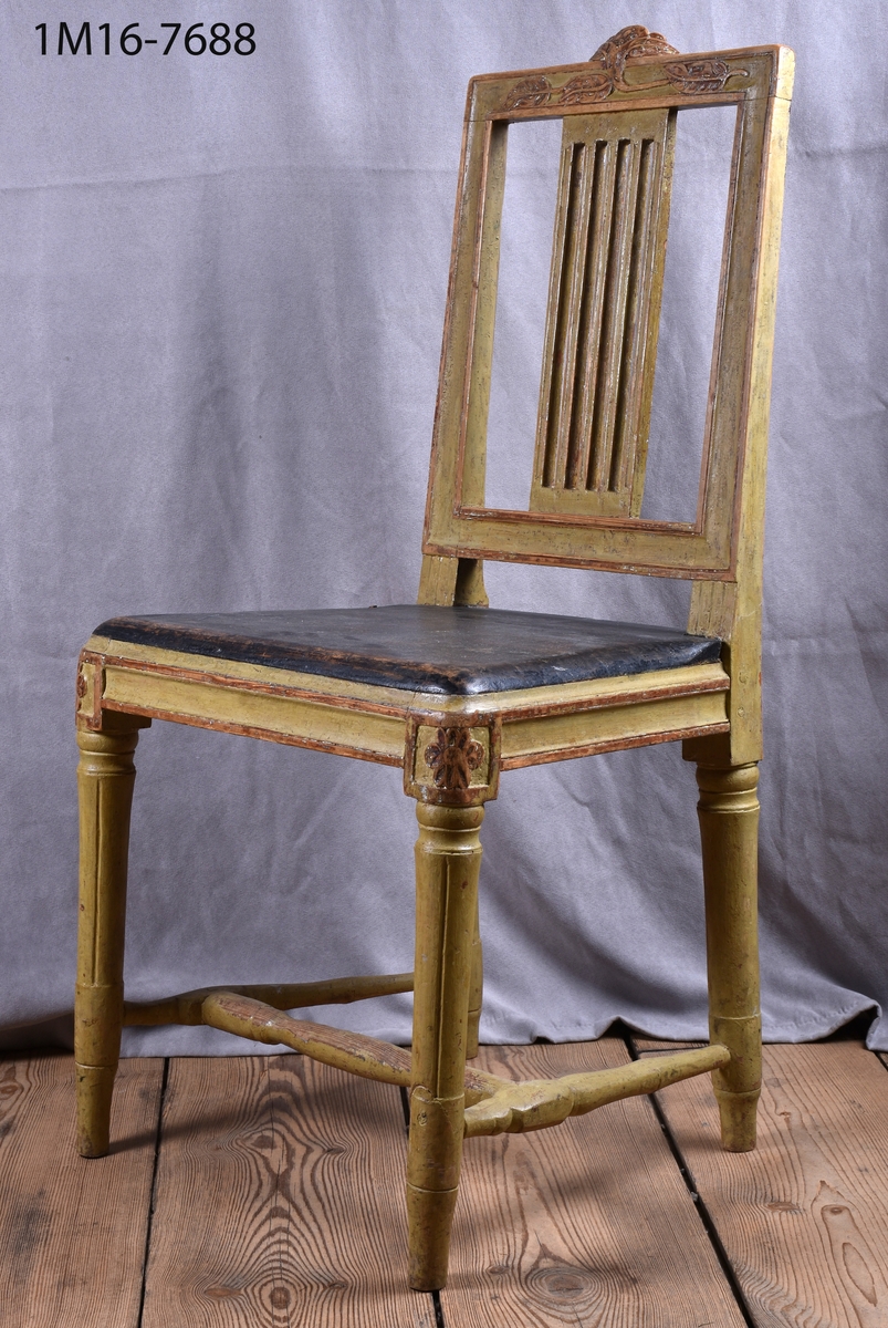 Gråmålad gustaviansk stol med svart sits, svarvade ben med kannelyrer, svarvat benkryss. Genombruten rygg med 4 st spjälor, skuret krön med blomm och bladmönster.