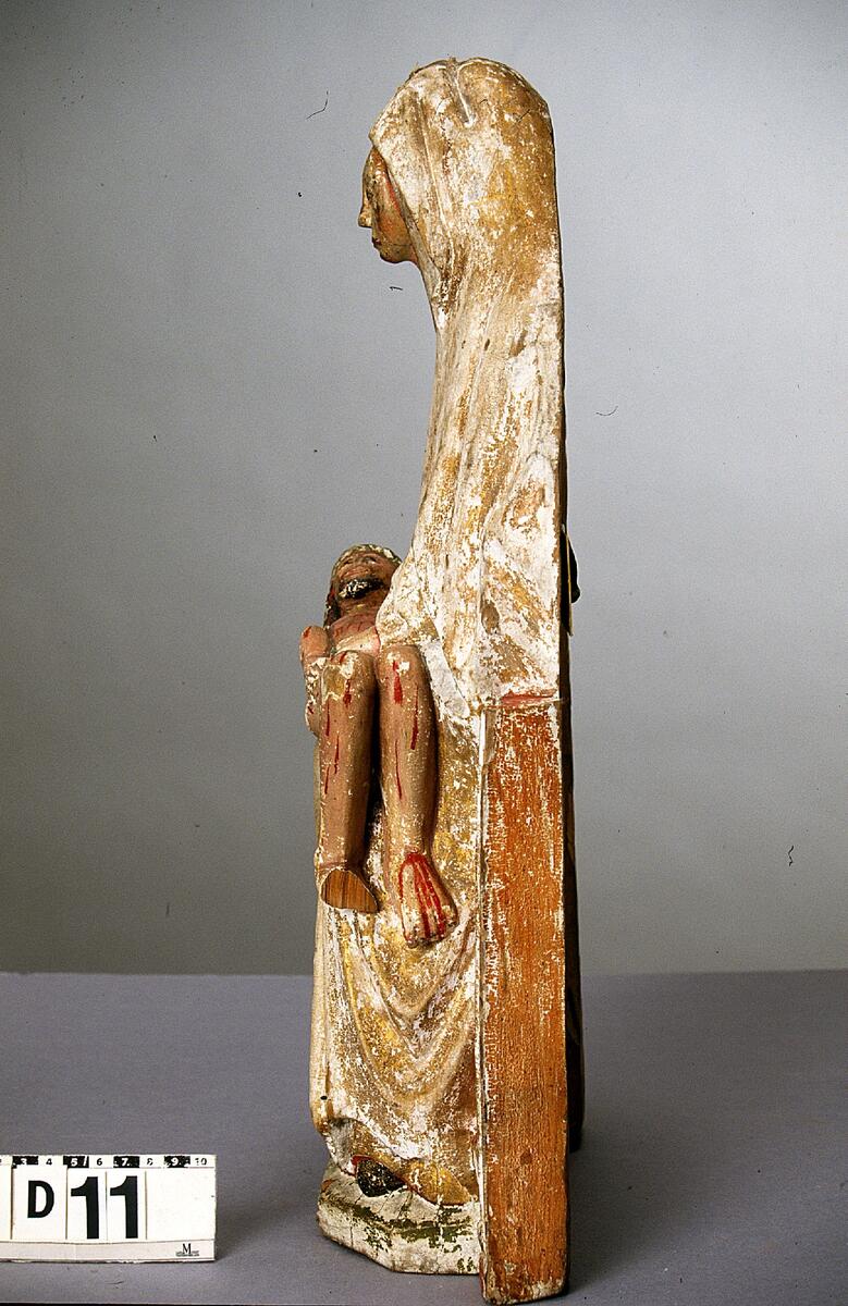 Pietà, Marie klagan. (Maria sörjande den döde Kristus, som är lagd öfver hennes knä). Träskulptur. Maria sittande å bänk med Kristus i liggande ställning i knät.(Marias huvud ovanligt litet i förhållande till kroppen i ö.) Marias dräkt i guld liksom den från huvudet nedhängande manteln. Kristi kropp heltäckt med sår, kring huvudet vriden törnkrona. H.47 cm. Omkr. 1525.  \"Pietà. 1520- eller 30-talet. Denna bild har rätt stor liket med altarskåpsfigurerna i Junsele. Torde vara utförda af någon provinskonstnär. H. 46 cm. Maria sitter på en enkel stol och håller den från korset nedtagne Kristus i sitt knä. Maria är klädd i en lång klänning och mantel. Klänningen är rakt avslutad vid halsen. Klänningens ursprungliga färger har varit guld på utsidan och röd på insidan. Den röda färgen syns vid klänningens kanter, både vid ärmarna och fötterna. Manteln täcker Marias huvud, faller ner på axlarna och sveper om kroppen ända ner till fötterna. Manteln har varit guldmålad på utsidan och blå på insidan. Några fallande veck uppstår vid Marias knä där hon särar på benen för att kunna hålla Kristus kropp. Marias fötter är klädda i svarta skor. Maria håller sin högra hand under Kristus huvud och nacke, den vänstra vid hans midja. Händerna är gråa med röda konturlinjer mellan fingrarna. Naglarna är svarta. Marias ansikte har en hög panna, en stor näsa, ett par halvslutna ögon och en rakt formad tunn mun. Ansiktets målning är fortfarande kvar. Ansiktet är inramat med en svart konturlinje. Ansiktets rosiga kinder kontrasterar mot den ljusgrå huden. De halvslutna ögonen har svarta ögonpupiller. Ögonen och även ögonfransarna är målade med svarta linjer. Munnen är målad med ett rött streck över den tunna överläppen. Marias ansikte är fullt av sorg och betänksamhet.; Kristusfiguren är alldeles naken. Han ligger i Marias knä med böjda ben. Hans högra hand ligger på kroppens högra sida, den vänstra är vänd mot Maria. Kristi bröstkorg är enkelt målad med svarta linjer i tjocka penseldrag. Kroppen liksom ansiktet är stänkt med röda bloddroppar på något ljusrosa hy. Ansiktet har ett svart målat skägg runt en halvöppen mun. Munnen är vit med röda tvärlinjer. En rödbrun konturlinje sträcker sig runt läpparna. Kinderna är röda. Näsan är avslagen. Ögonen är öppna med målade svarta pupiller och konturslinjer med ögonfransar. Ögonbrynen är mörkbruna med målade enstaka hårstrån. En törnekrona i grön färg sitter på Kristus svarta hår. Håret är långt och ligger över nacken. Den avlånga halsen är målad med rosa färg.; Maria sitter på en stol som liknar en väggbänk. Stolen är målad med grön färg längst upp och längst ner, röd färg i mitten och guld vid kanterna. Sidostyckena är röda och gula. Marias fötter vilar på en fotbräda, ursprungligen grönmålad. Stil och datering: Pietàbilden blev mycket populär under 1300- och 1400-talen i Europa. Pietà från Sättna är ovanlig i sitt stilistiska utförande. Kroppens utformning och proportioner är felaktiga. Kristus kropp är onaturligt utformad med felböjd höger arm och hand. Hans vänstra hand är felvänd mot Marias kropp. Marias vänstra hand har fyra fingrar lika långa. Hennes hals är avlång och ansiktet för litet i förhållande till huvudet. Marias kropp är också för stor till den lilla Kristuskroppen om den ska föreställa en vuxen människa. Det är möjligt att man vill föreställa Maria med den döde Kristus förvandlad på nytt till ett barn. En sådan pietàframställning har funnits på medeltiden. Att så är fallet understryks av Kristus nakna kropp.; Skulpturen är ganska ovanlig på grund av dessa naiva drag. Men det finns en hel del andra skulpturer i Norrland som har samma stilistiska drag som denna pietà från Sättna. TEKNISK BESKRIVNING; Baserad på okulär beskrivning. Pigmenten är identifierade genom jämförelse med uppstrykningar av kända pigment. Bindemedel är identifierade med löslighetstest. Träslagen är identifierade genom jämförelse med en provsamling kända träslag. 2002LK. Dimensioner:; Höjd: 47,5 cm; Bredd: 25 cm; Djup: 12 cm; ; Pietàskulpturen är utformad som halvskulptur  och skuren i ljust lövträ i ett stycke. Skulpturen har en grund V-formad urholkning på baksidan (höjd:30 cm och djup: 5 cm). Skulpturen har spår av ett rakt eggverktyg på baksidan (bredd: 6 cm) och en avsågad tapp på hjässan (diameter: 1,2 cm). På skulpturens baksida finns en stor järnspik. Skulpturens framsida är grunderad med animaliskt lim och krita. På några ställen är ojämnheter i underlaget utjämnade med linneväv. Karnationen på Maria och Kristus är rosa och tonad mörkare vid hårfäste, ögonlock, halslinning m.m. Iris, pupiller och naglar är svarta. Kristus hår har ristningar i grunderingen och är målad med brunt, törnekrona är målad med kopparresinat. Blodflödet på Kristus är målad med cinnober. Utsidorna på Marias mantel och tunika är förgylld med polerat bladguld. Mantelns insida är målad i azurit i limfärg på svart undermålning. Tunikans insida är röd. Marias skor är svarta. Tronen är förgylld med polerat bladguld och bemålad med cinnober och kopparresinat. Tronens utsida har orange bemålning. Marksockeln är målad med kopparresinat. Från Sättna k:a Medelpad 1912
