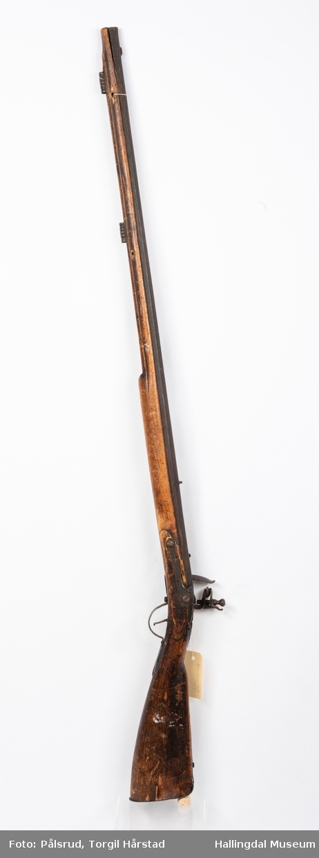 Gevær med eldre militær flintlås. Privat våpen med riflet løp. Mulig satt sammen tidlig 1800-tall.
Utskjæringer i treet bak lås. Mangler ladestokk. Ornament under lås og på kolbekappe.