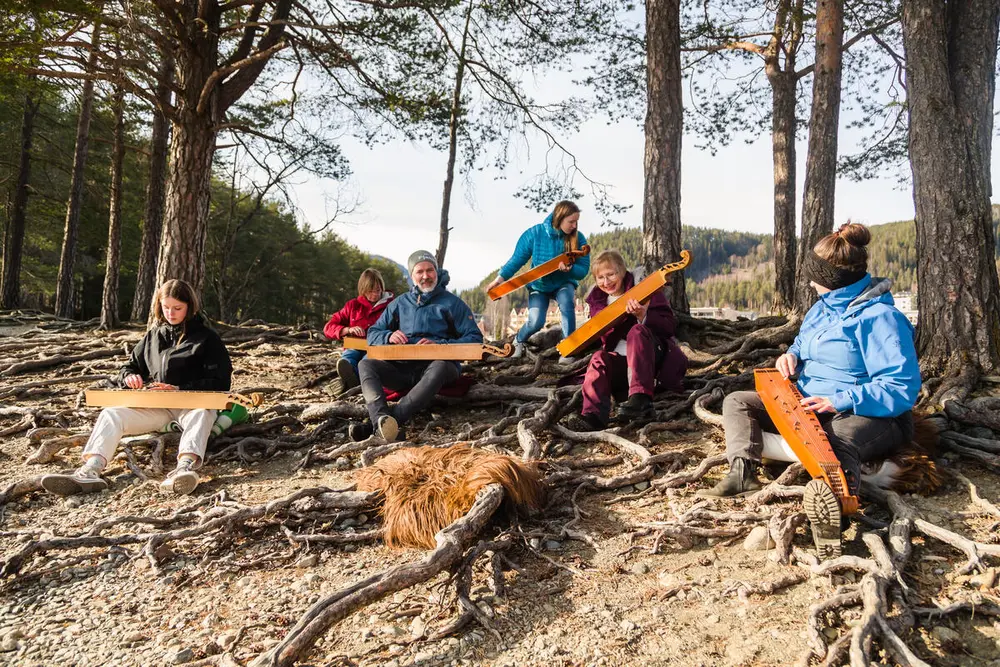 langeleikspelarar som sitter ute i naturen