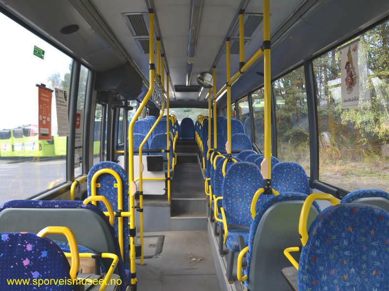 Grønn og svart buss med enkeltdør i fremme og dobbeltdør i midten. Interiøret består av grå overflater og blå seter. 
