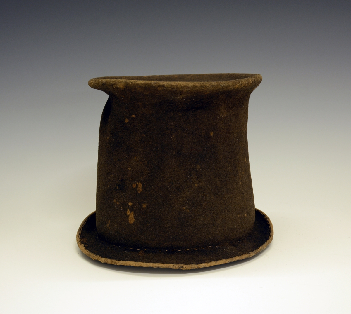 Hatt. Brun hatt laget av filt, høy pull og smal brem rundt hele formen.