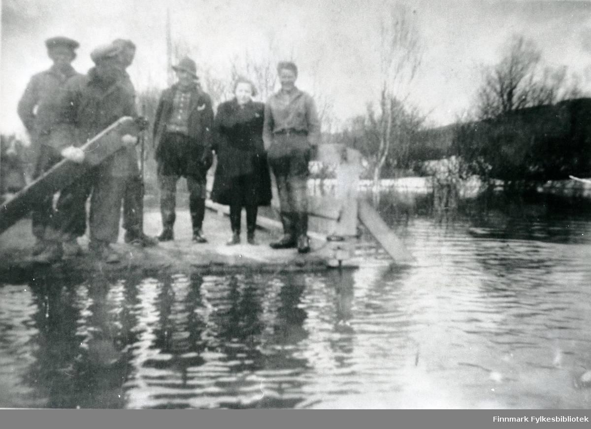 Fem menn og en dame står på en bru eller veien som vårflom har tatt over i 1946, i Tana.