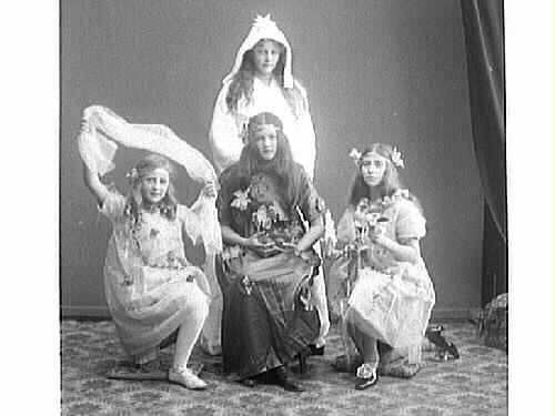 Fyra flickor troligen utklädda till de fyra årstiderna: Vinter i stjärnprydd kåpa, höst sittande med fruktskål och löv på dräkten, sommar med solfjäder och vår med blomor och skir slöja till vänster.
(Se även bild MR2_1330, 1331)